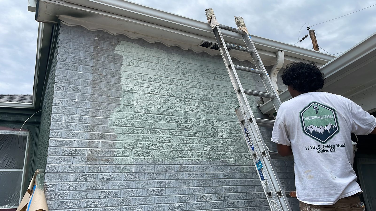 Alvarez crew member on an extension ladder painting a brick gable wall